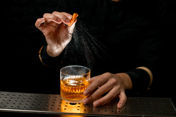 Close-up bartender's hand sprinkle to alcoholic cocktail with piece of citrus zest