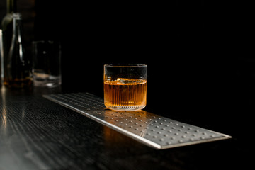 View on old-fashioned glass with amber alcoholic drink which standing at bar counter.