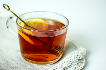 A transparent mug with black tea, a slice of lemon, a spoon for honey on a wicker gray napkin on a light table. The concept of a cozy tea party. Close-up