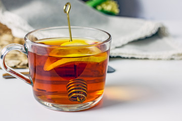 A transparent cup with black tea, a slice of lemon, a spoon for honey on a wicker gray napkin on a light table. The concept of a cozy tea party. Lemon tea in a cup. Close-up