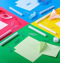 Stationery and paper origami toys on the multicolored geometric background. Creative flat lay