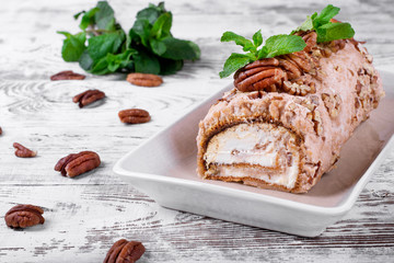 Meringue roulade with pecan nuts and cream cheese filling on the ceramic platter on the white wooden table