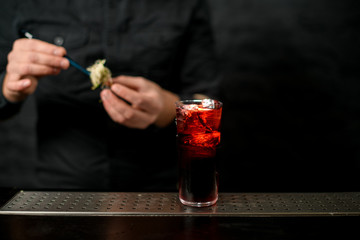 Close-up old-fashioned glass with red alcoholic drink standing at bar counter.