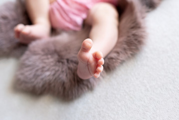 Feet of the newborn baby. pink color. mother's day. little girl in pink bodysuit lies on brown rabbit fur