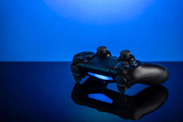 Black gamepad with backlight on blue back. Joystick on glossy surface.