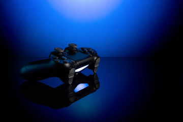 Black gamepad with backlight on blue back. Joystick on glossy surface. © solidmaks