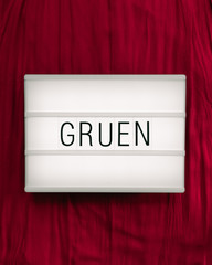 Leuchtkasten mit dem deutschen Wort "Grün" auf bordeauxrotem Hintergrund zum Ausdruck eines Kontrasts; komplementär, flat lay