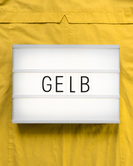 Leuchtkasten mit dem deutschen Wort "Gelb" auf sonnengelbem Hintergrund; flat lay, von oben