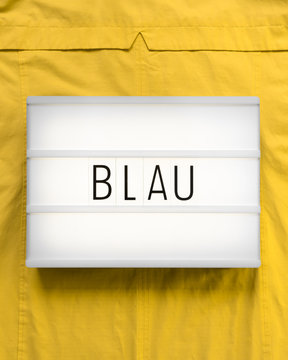 Leuchtkasten mit dem deutschen Wort "Blau" auf sonnengelbem Hintergrund zum Ausdruck eines Kontrasts; komplement&auml;r, flat lay