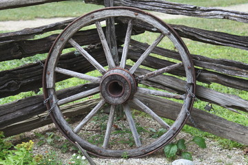 Fototapeta na wymiar WOOD WHEEL, SHAPE, WAGON, RUSTIC IN COLOR, NEXT TO A OLD FENCE