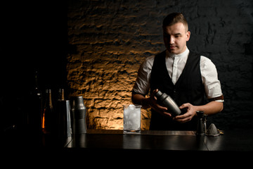 Bartender with shaker in his arms stands behind bar.