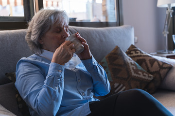 Woman drinking tea sitting on a couch with expression of pleasure