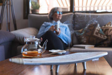 Glass tea kettle steaming and a woman drinking tea in the background