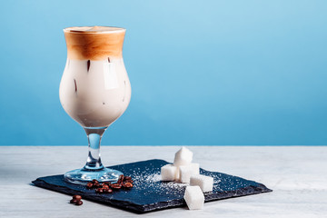 Dalgona korean Iced Coffee, a trendy fluffy creamy whipped coffee with ice on a white wooden table. trendy coffee drink on a blue background