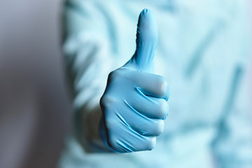 Doctor in a dressing gown and medical gloves shows thumb up.