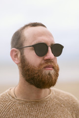 young man with beard and glasses on beach near sea
