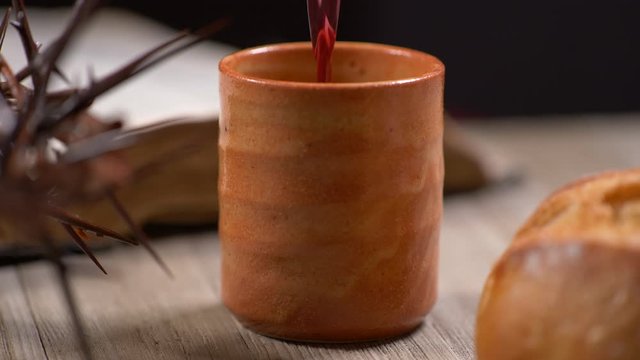 Cup being filled with wine with Crown of Thorns and old Bible and bread