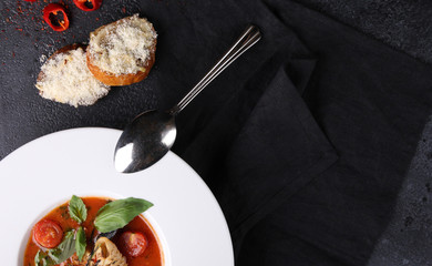 Italian cuisine. Cacciucco, seafood tomato soup in a white plate with basil, a spoon and croutons on a black background. Restaurant menu. Top view, flatlay. Background image, copy space
