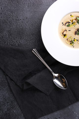 Mushroom cream soup with herbs and spices in a white plate with spoon on a black background. Restaurant menu. Top view, flatlay. Background image, copy space