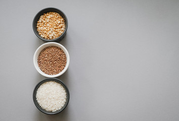 Containers of grain products, buckwheat, rice and peas in storage jars on the grey background