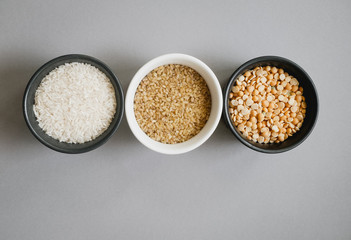 Containers of grain products, bulgur, rice and peas in storage jars on the grey background.