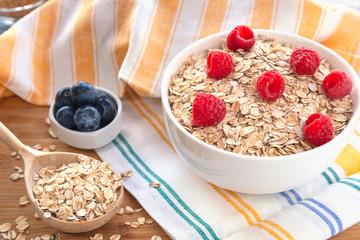 Bowl of muesli, raspberry and blueberries for healthy breakfast. Tasty breakfast with oatmeal and natural berries and pastel background.