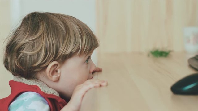 Сute little kid licks the table while watching TV. Young boy with blue eyes watch television on living room. Child watching TV, close up face of little boy, kid eyes.