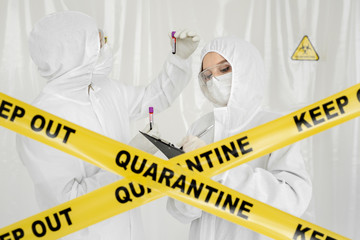 Epidemiologist woman in protective clothing is in a restricted area with a planchette. Infected...