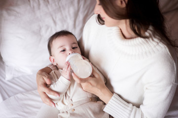 Mother feeding baby boy with milk in plastic bottle in bed closeup. Childhood. Motherhood. Healthy...