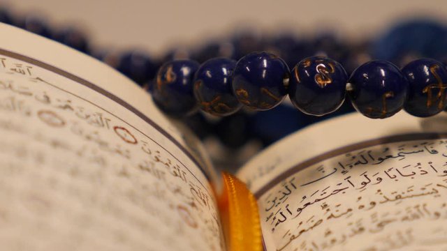 Close up footage of a Quran and a prayers bead near it-the shgot is moving in a half circle