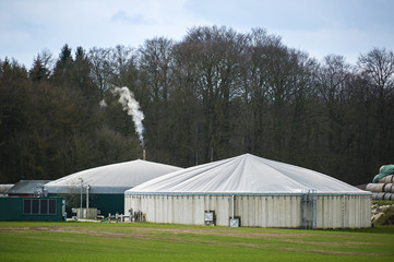 Biogas plant with smoking chimney at the edge of a  forest, cloudy sky, copy space