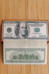 A large wad of American dollars is lying next to a wooden box