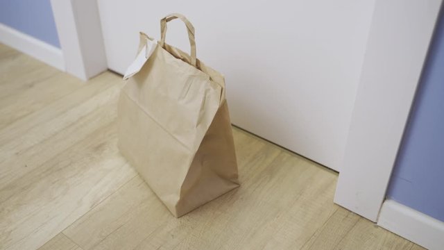 Hand with latex glove sets take-out food paper bag by door - no contact delivery