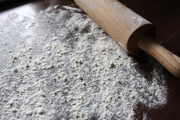 Baking cake - wheat flour scattered on a brown kitchen countertop with wooden roller pin