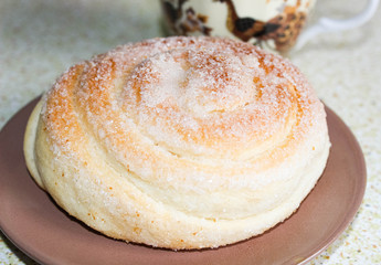 A pastry bun sprinkled with sugar on top lies on a saucer.