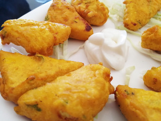 Close up paneer cheese fried in batter is on a platter with white sauce and herbs
