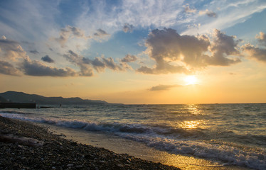 Amazing sea sunset on the pebble beach, the sun, waves, clouds