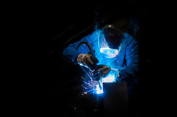 Man welding in a fabric with sparks, dark background