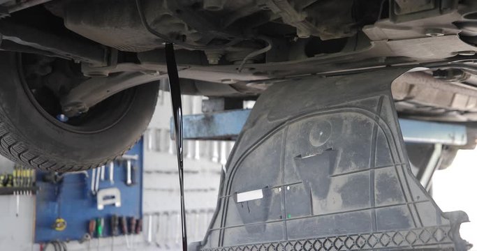 Footage of a car on a crane at the mechanic-the mechanic is releasing old oil from the engine