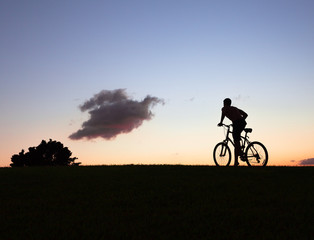 Fototapeta na wymiar Silhouette of man biking through countryside at sunset. 