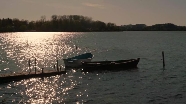 Boote liegen am Steg im See. helles sonniges Funkeln auf der Wasseroberfläche und leichte Wellen im Abendlicht.