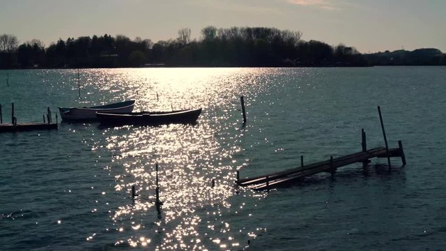 Boote liegen am Steg im See. helles sonniges Funkeln auf der Wasseroberfl&auml;che und leichte Wellen im Abendlicht.