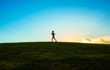 Obraz na płótnie Canvas Woman running, jogging up a hill at sunset. 