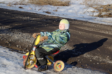 a little boy rejoices in the spring sun, rides a tricycle on a clear sunny day.