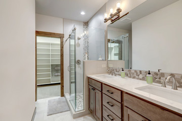 Natural new classic bathroom interior with two sinks and walk in glass shower, large walk in closet.