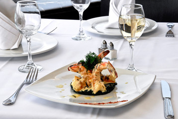 plato de camarones asados a la mantequilla con copa de vino blanco, sobre una mesa de restaurante, con vista panorámica a la ciudad y mantelería blanca  