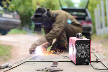 Old man welder in brown uniform, welding mask and welders leathers, weld metal door with arc...