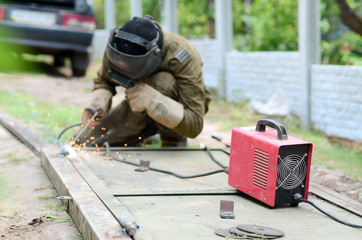 Old man welder in brown uniform, welding mask and welders leathers, weld metal door with arc...