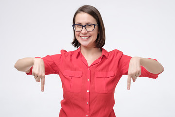 Young woman points down with forefinger , isolated on white wall