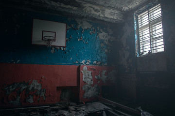 Fototapeta na wymiar View of the ruined gym with a basketball hoop and light from a window at a school in Teriberka. Like after the war. Apocalypse.